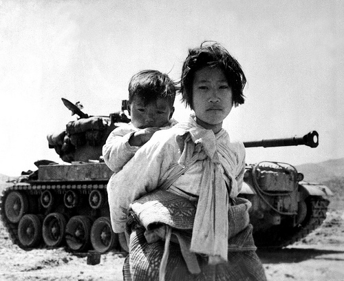 With her brother on her back a war weary Korean girl tiredly trudges by a stalled M-26 tank, at Haengju, Korea. June 9, 1951. Maj. R.V. Spencer, UAF. (Navy)